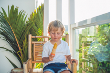 Cute little blond boy eating a homemade icecream sitting on a wooden chair